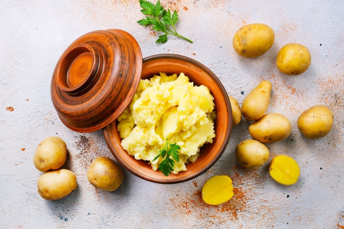 Fluffy mashed potatoes in a decorative bowl feature alongside ripe Yukon Gold potatoes scattered about.